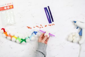 adding a felt scarf to a snowman made from pom poms