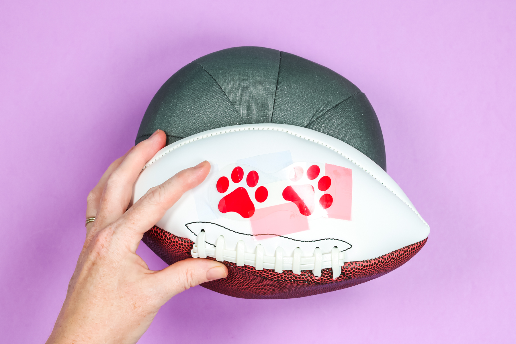 Cricut Hat Press form with deflated football and paw print HTV decals and heat-resistant tape.
