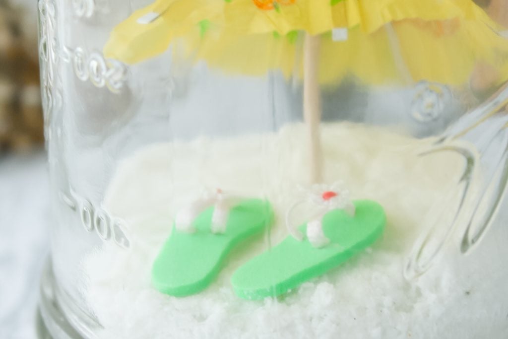 mini flip flops on sand in a mason jar