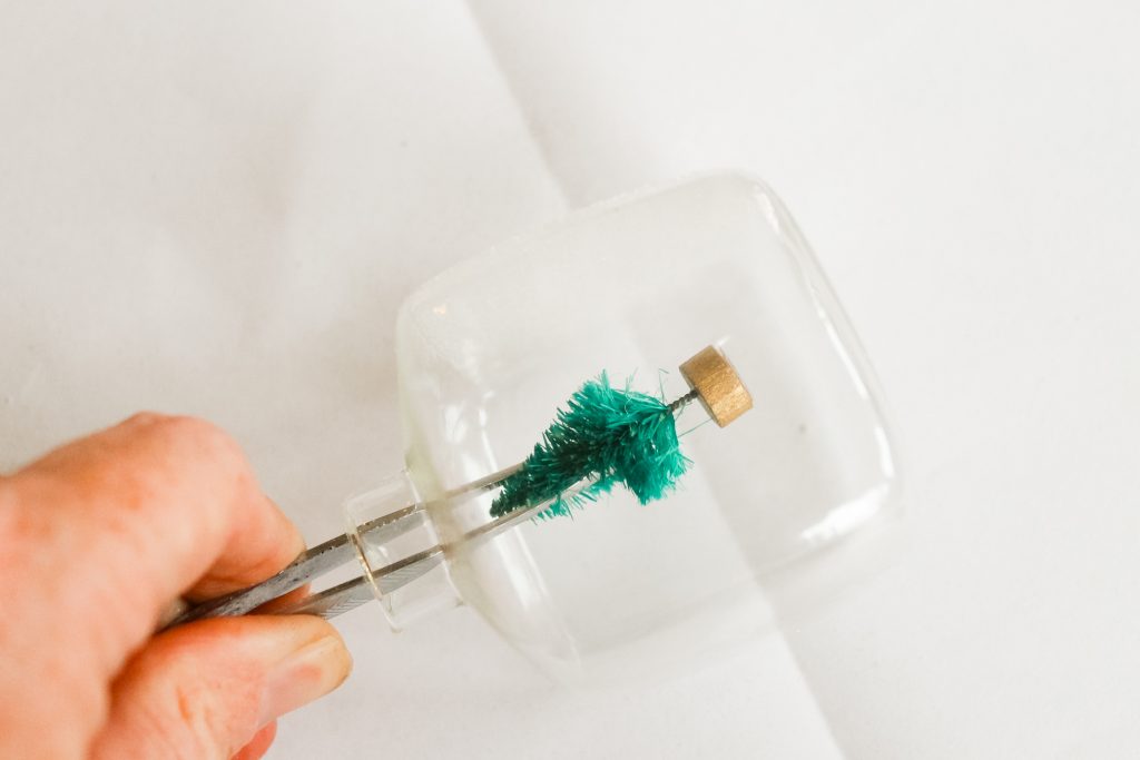 Kids Craft: Mini Snow Globe Ornaments -- click the picture to get the full instructions for making your own fun Christmas ornaments. adding tree to an ornment with tweezers and hot glue